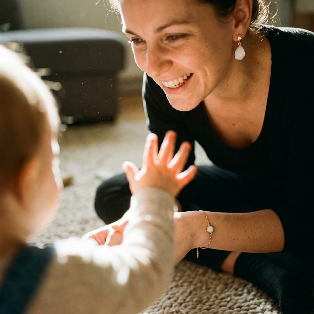 Smiling mom playing with her baby on the floor while wearing breastmilk keepsake jewelry earrings and bracelet, a meaningful 1 year breastfeeding gift to celebrate motherhood.