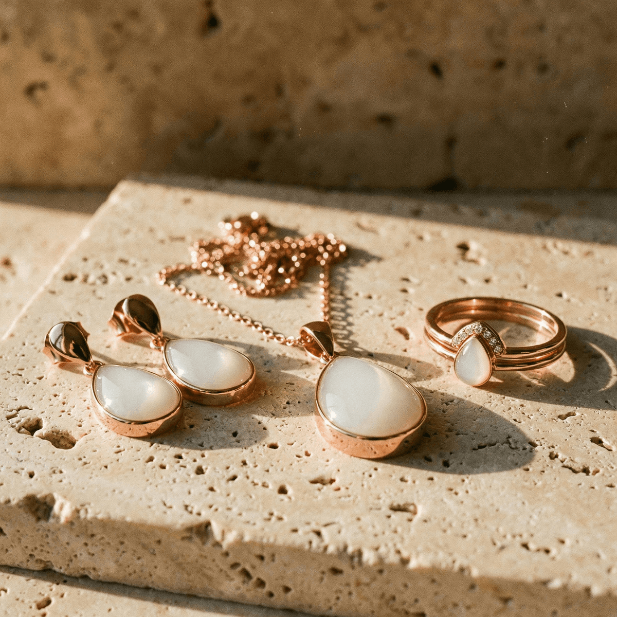 Rose gold breastmilk jewelry set styled as a 6 months breastfeeding award keepsake, featuring a teardrop pendant necklace, matching earrings, and ring on a textured stone surface