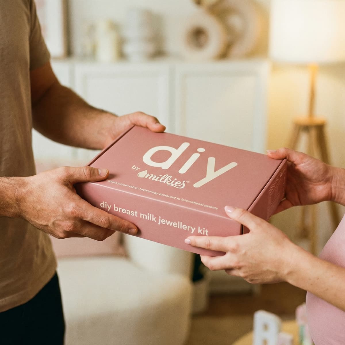 Hands exchanging a pink DIY by MILKIES breast milk jewellery kit box, a thoughtful breastfeeding gift for creating a keepsake at home.