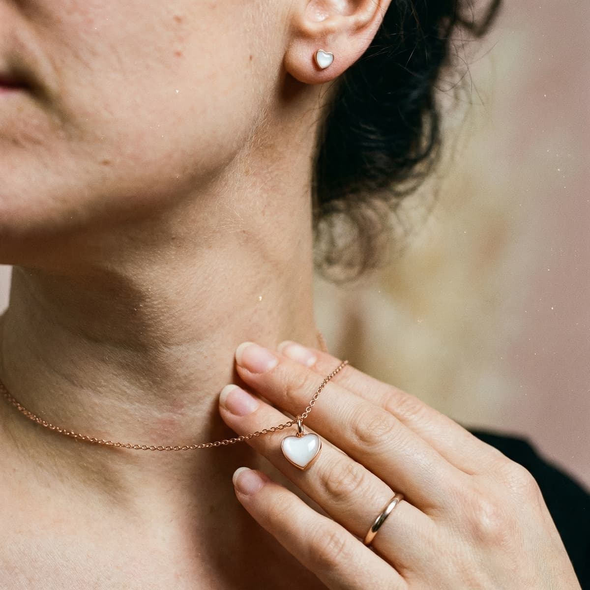Close-up of a woman wearing a rose-gold heart pendant necklace with matching heart stud earrings, a meaningful breastfeeding journey gift keepsake.