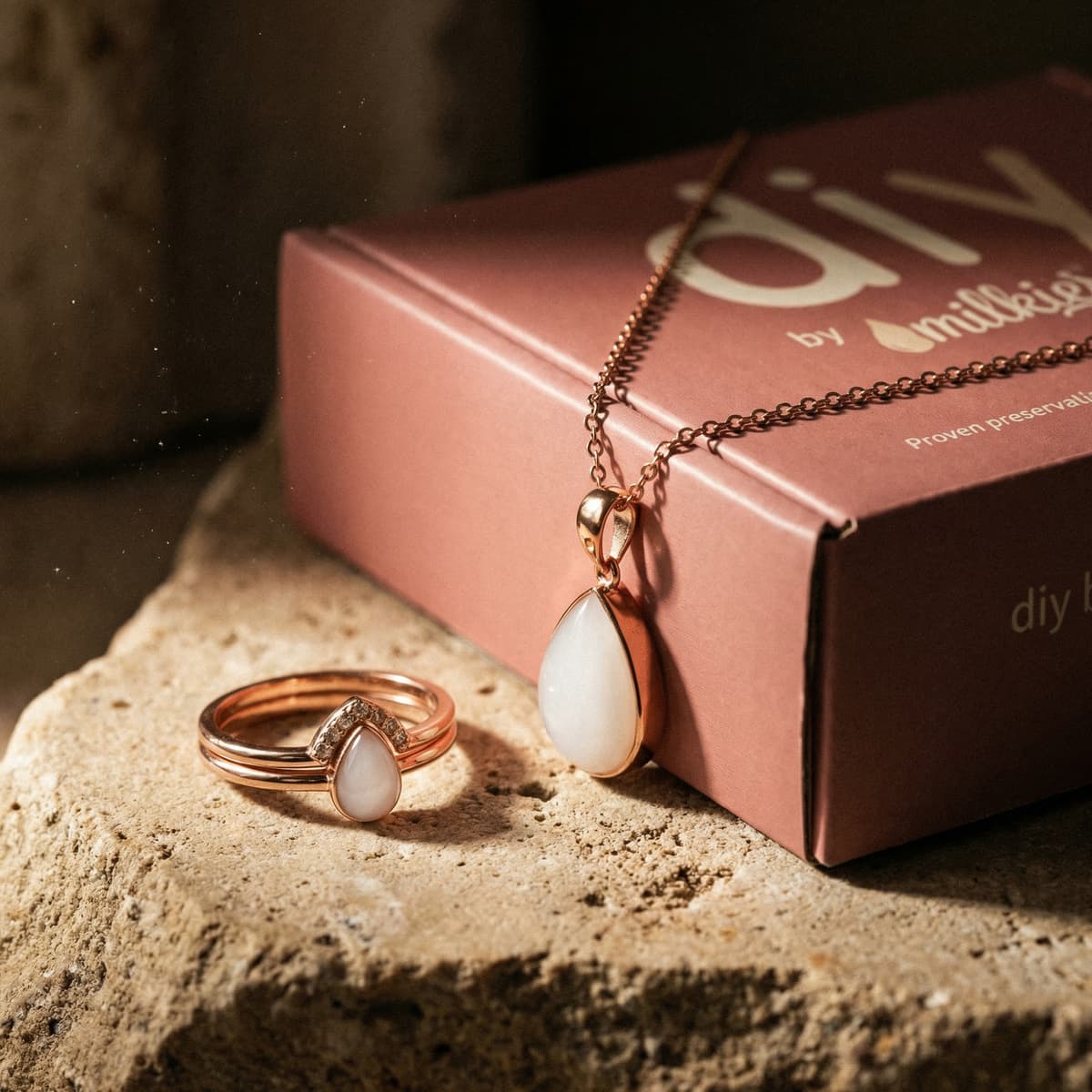 Rose gold necklace and ring with teardrop white resin stones beside a pink DIY by MILKIES breastmilk keepsake kit box, a meaningful breastfeeding journey gift for moms.