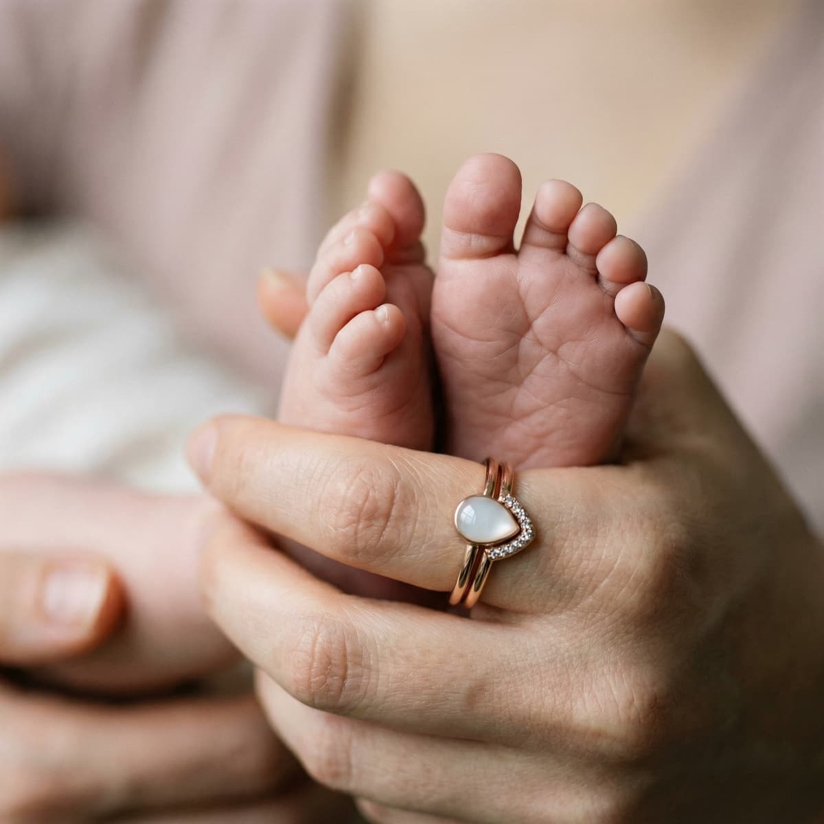 Mother holding newborn’s feet while wearing a milky white breastmilk ring in a rose-gold heart setting with tiny stones, a sentimental breastfeeding keepsake jewelry piece.