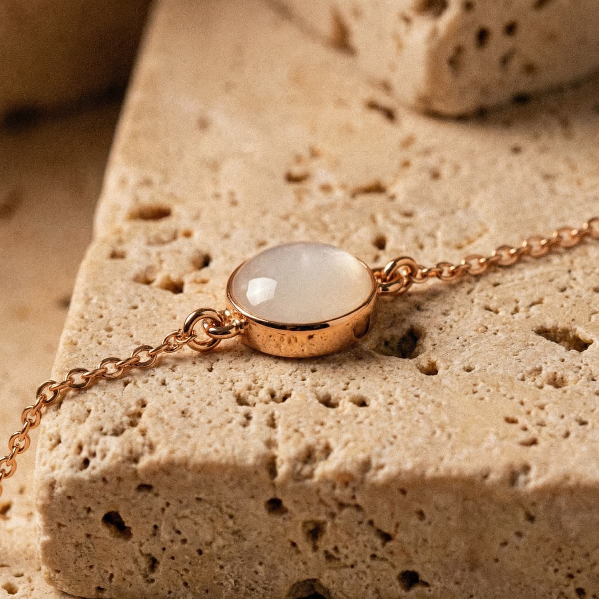 Rose gold chain bracelet featuring an oval breastmilk stone in a polished bezel, a keepsake breastmilk bracelet photographed on a textured beige stone surface.