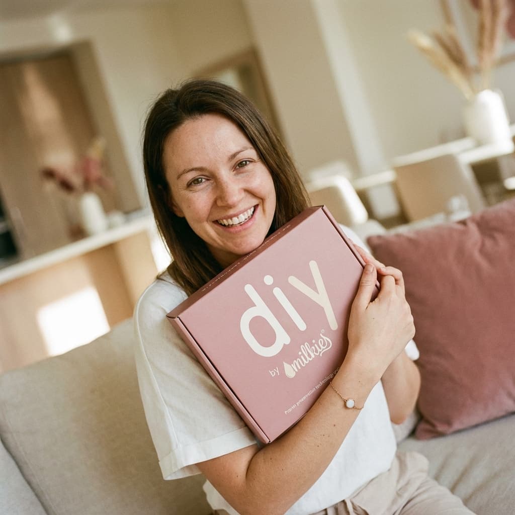 Smiling mom at home holding a DIY by MILKIES box, showing how this breastmilk bracelet kit lets mothers create a meaningful keepsake privately and conveniently themselves.