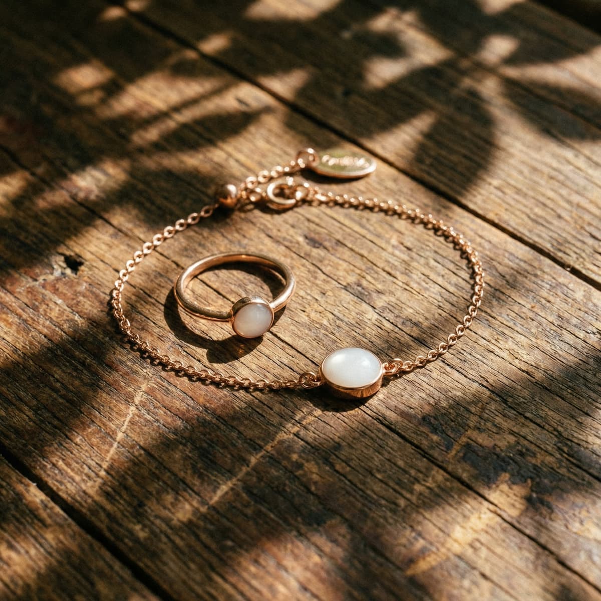 Delicate gold chain bracelet and matching ring with milky white resin stones, elegant breastmilk bracelets displayed on a rustic wooden surface in warm sunlight