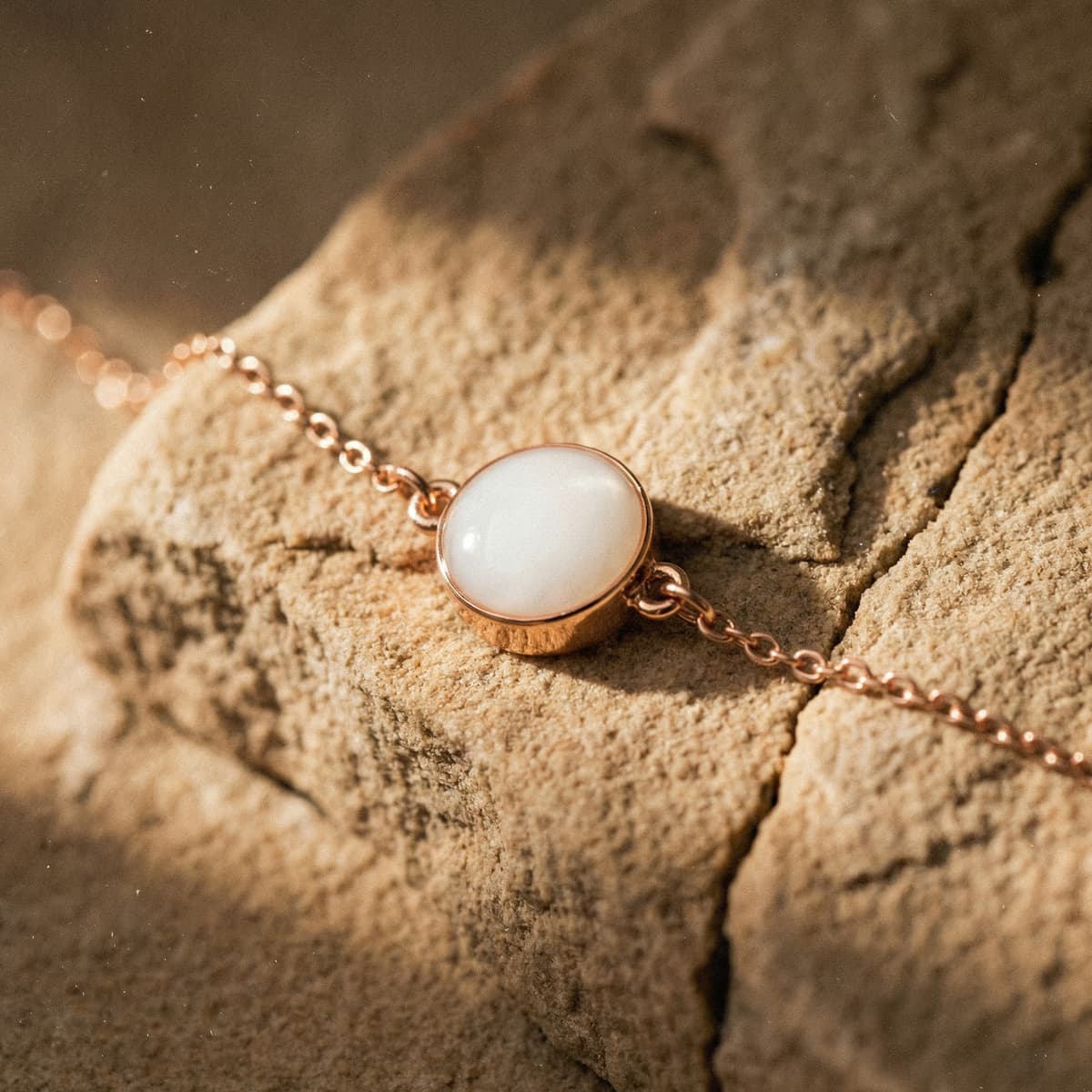 Minimalist rose gold chain bracelet featuring a round milky-white resin centerpiece, showcasing breastmilk bracelets keepsake jewelry on a textured beige background.