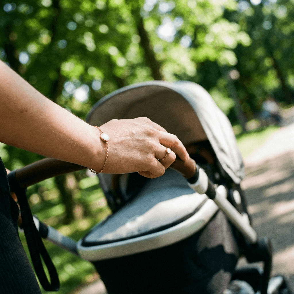 Mother pushing a stroller outdoors wearing a delicate gold keepsake bracelet made with a breastmilk bracelets kit