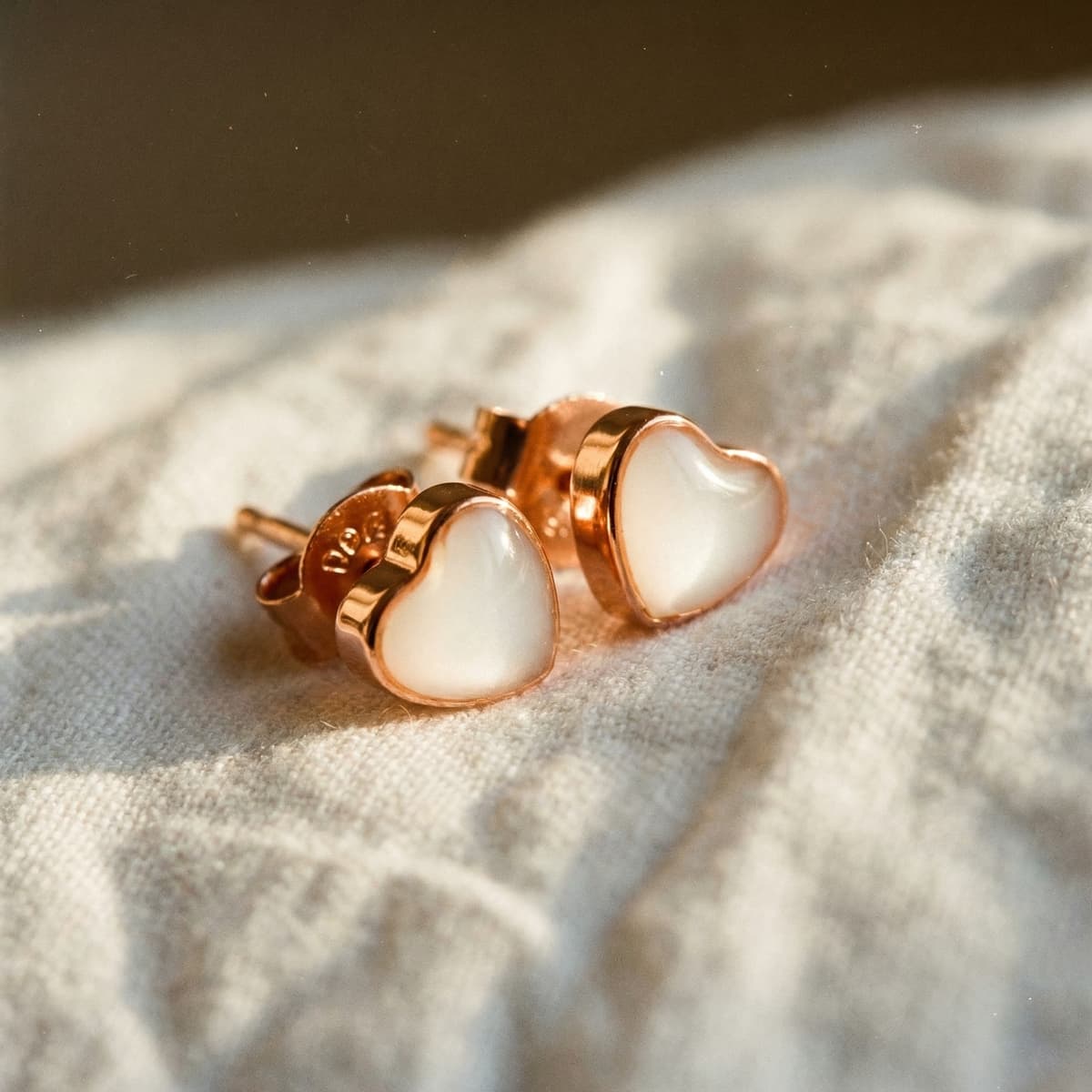 Heart-shaped rose gold stud earrings made with creamy white breastmilk resin, showing the finished keepsake from a breastmilk earrings diy kit on soft fabric.