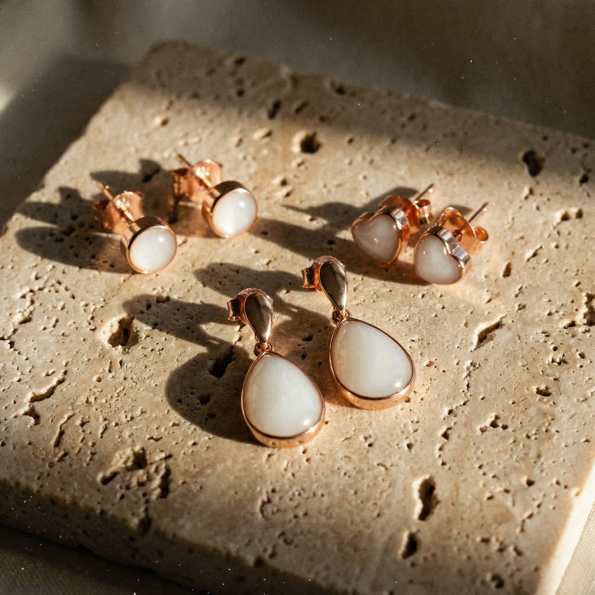 Rose gold keepsake jewelry on textured stone, including teardrop, heart, and round stud earrings crafted with a breastmilk earrings kit.