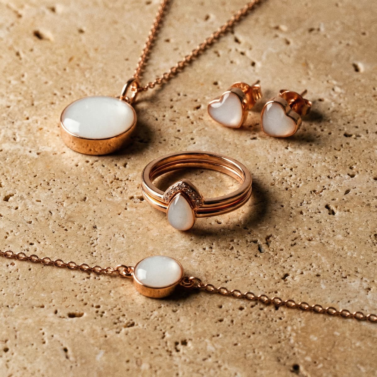 Rose gold DIY keepsake set shown as a breastmilk jewelry making kit, featuring a ring with teardrop stone, heart stud earrings, and matching white resin pendants on a textured beige stone background.