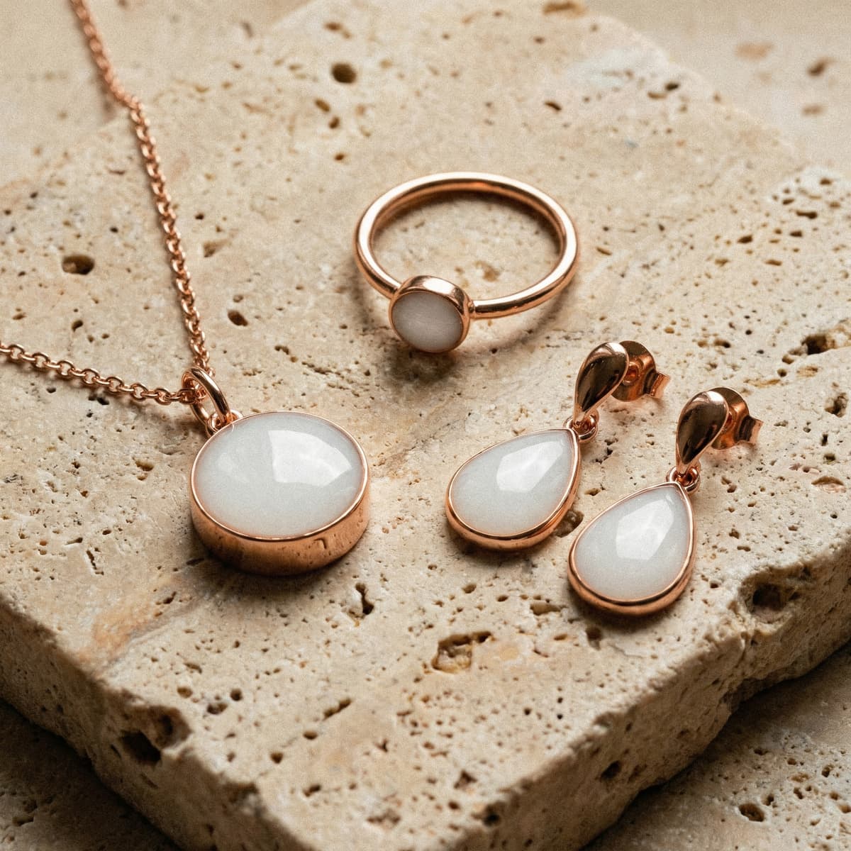 Rose gold necklace, ring, and teardrop earrings with milky white resin stones displayed on textured stone, showcasing finished keepsakes made using a breastmilk jewelry resin kit