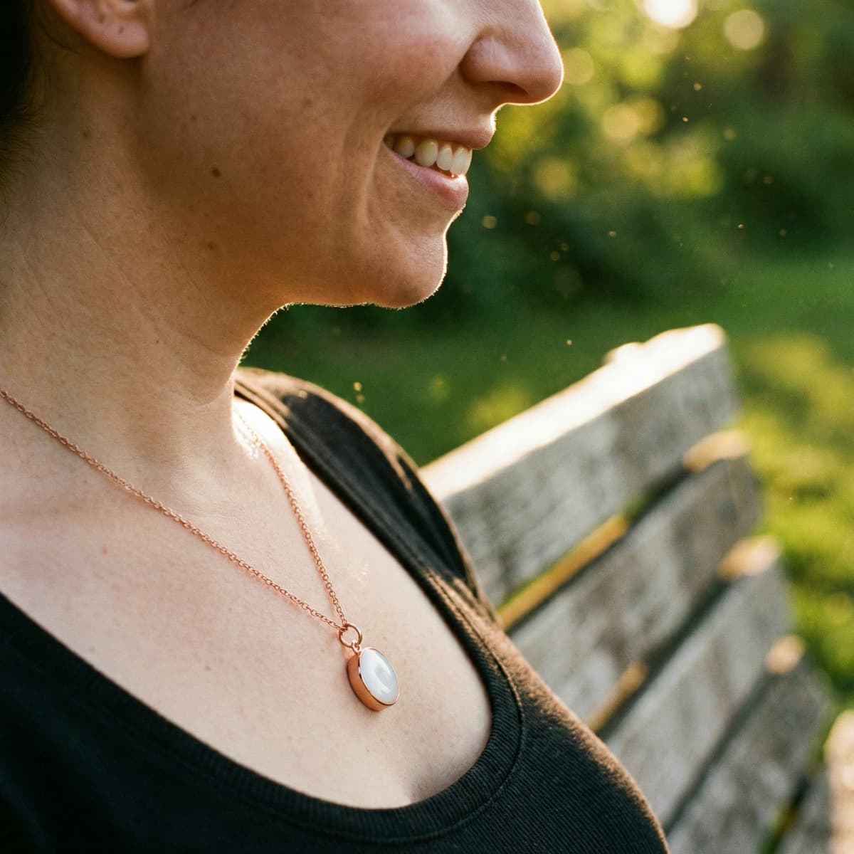Smiling woman outdoors wearing a rose-gold pendant made with a breastmilk necklace kit, featuring a milky-white resin breastmilk keepsake on a delicate chain.