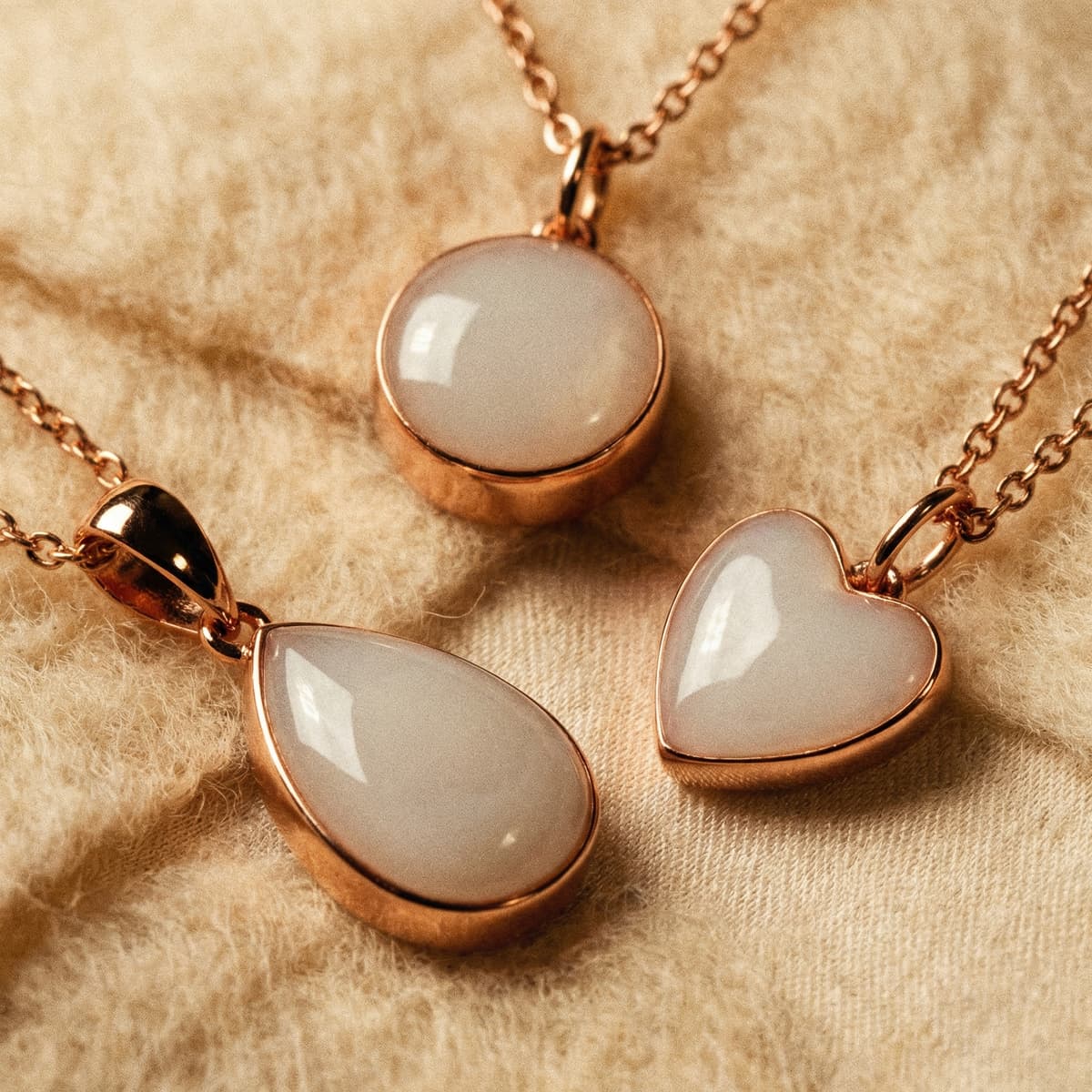 Rose gold pendants featuring teardrop, round, and heart milky white resin stones on soft fabric, showcasing elegant breastmilk necklaces keepsake jewelry.