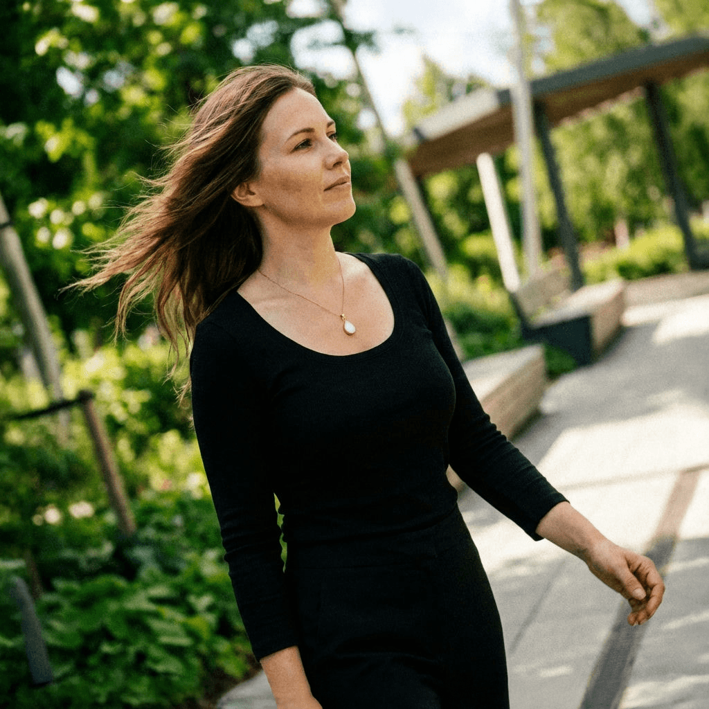 Woman walking outdoors in a black dress wearing a teardrop-shaped white keepsake pendant on a delicate chain, one of the breastmilk necklaces.