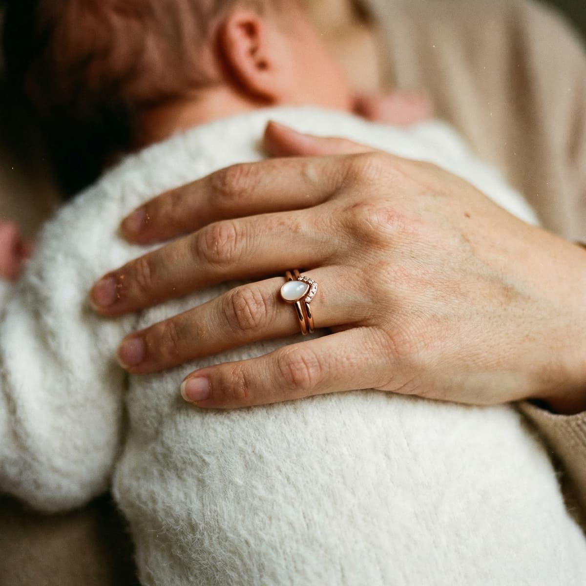 Mother cuddling her baby while wearing a rose-gold breastmilk ring with a milky white stone, highlighting why choosing the DIY by MILKIES at-home keepsake kit is meaningful and private.