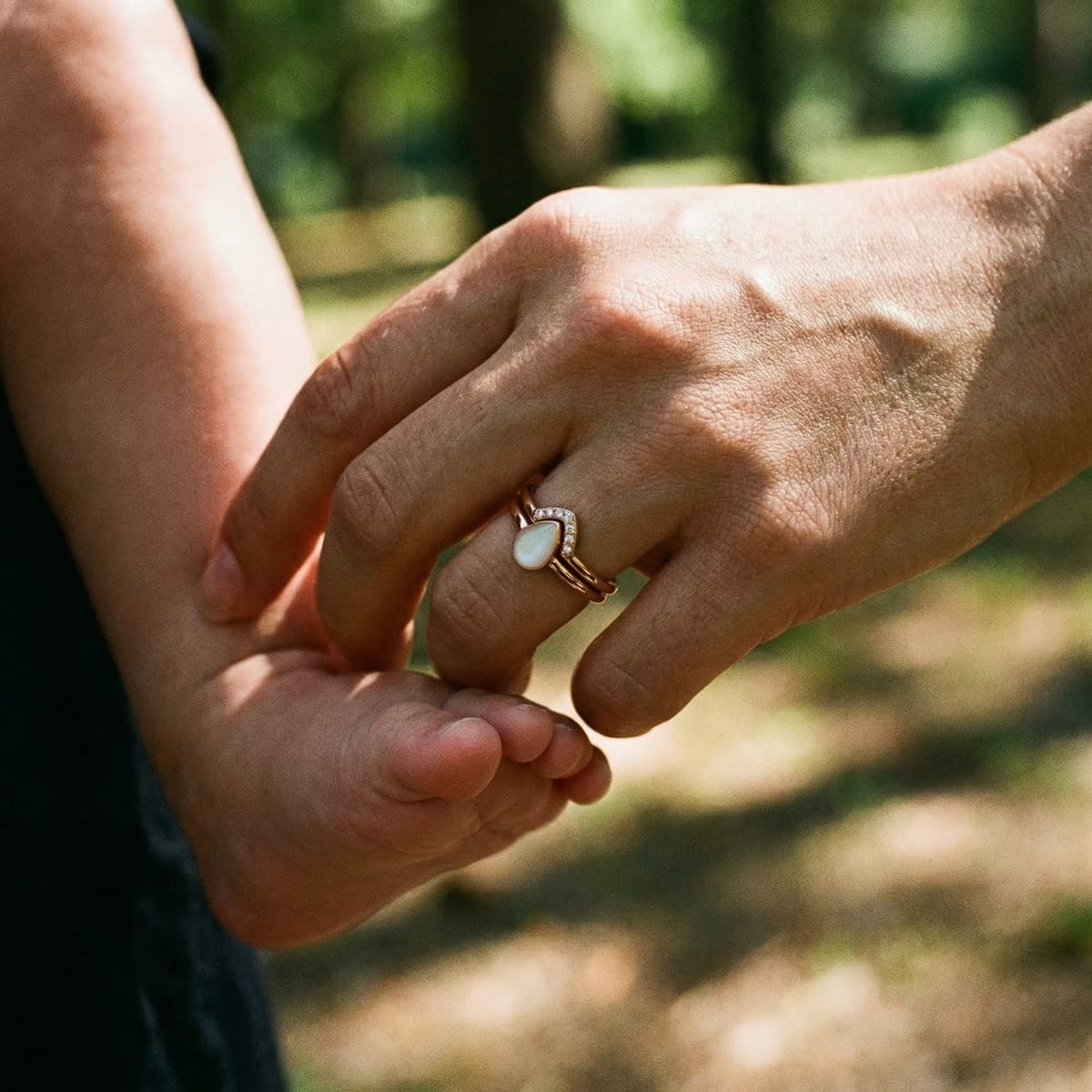 Mother holding her baby’s foot outdoors, wearing a rose-gold keepsake ring with a white stone made using a breastmilk ring diy kit in soft natural light.