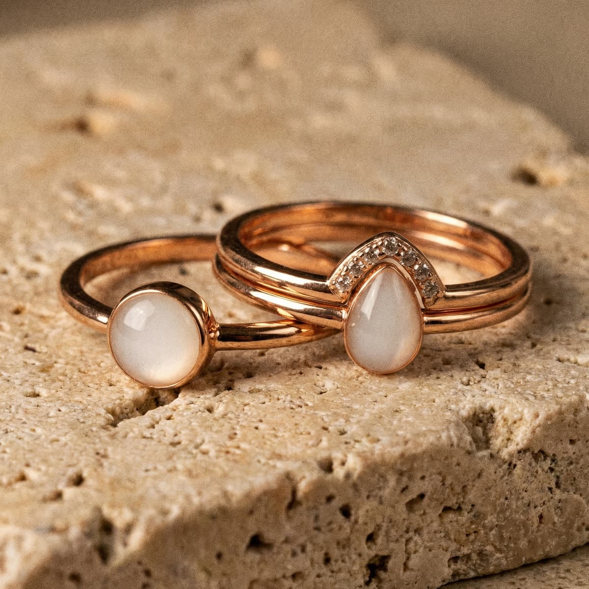 Two rose-gold keepsake rings with milky white resin stones made using a breastmilk ring kit, displayed on a textured stone surface.