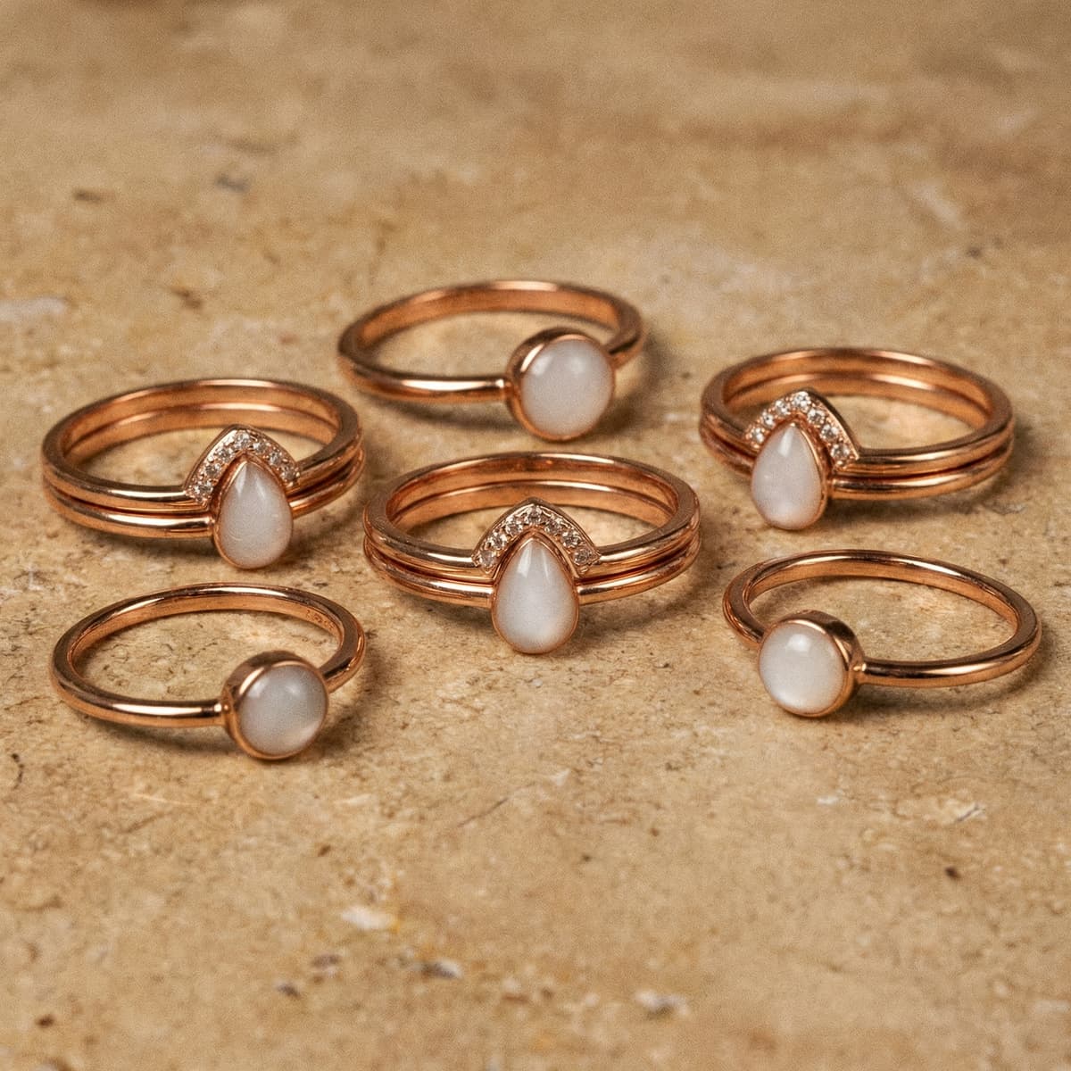 Rose gold rings with milky white resin stones displayed on a neutral stone background, illustrating keepsake jewelry you can create with a breastmilk ring making kit.
