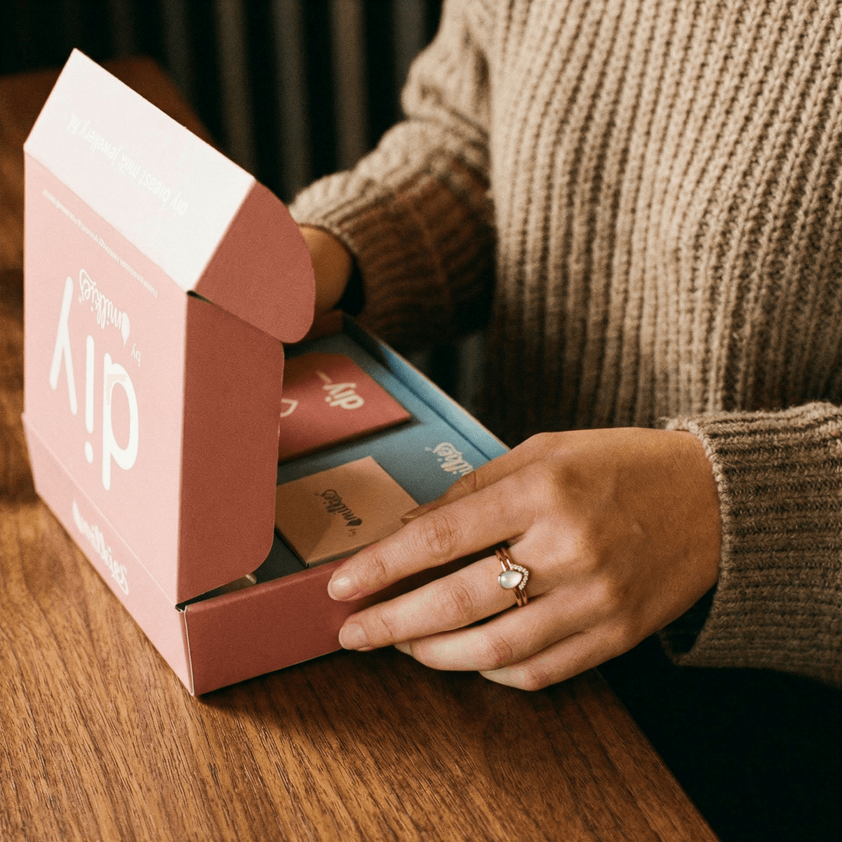 At-home DIY kit for making breastmilk rings opened on a wooden table, showing MILKIES tools and packaging for a private, hands-on keepsake experience.