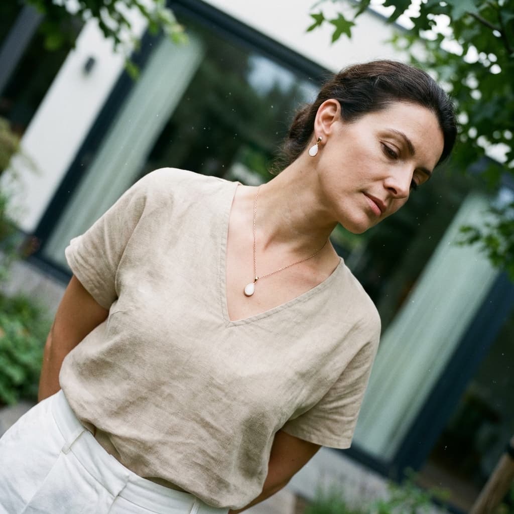 Woman outdoors wearing a delicate pendant necklace and matching earrings, showcasing diy breast milk jewellery keepsake pieces in a natural setting.