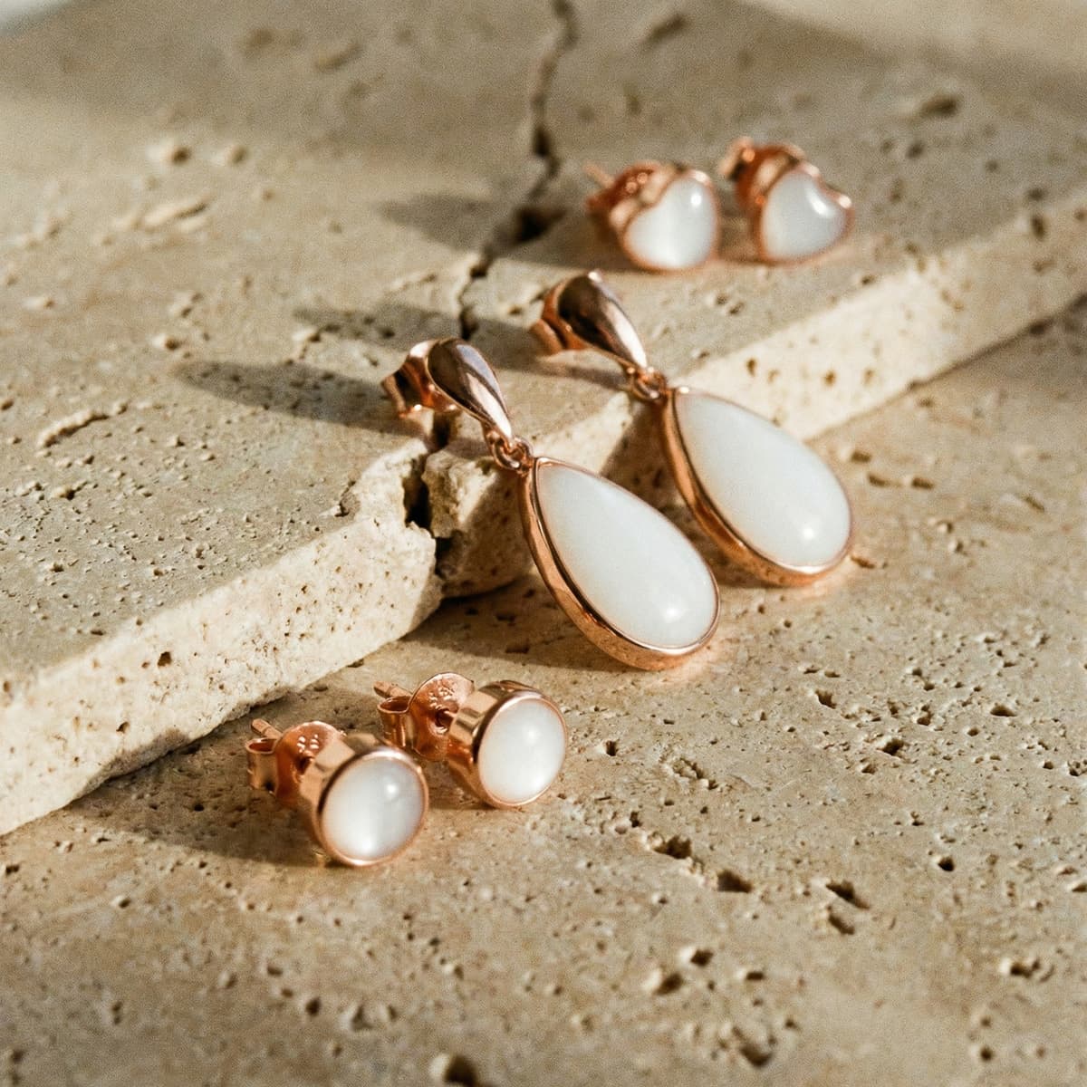 Rose-gold teardrop and stud jewelry set featuring a diy breastmilk earring design with milky white resin stones on a textured beige stone surface.