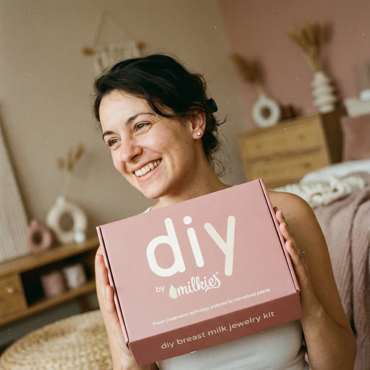Smiling mother holding a pink DIY by MILKIES kit box, highlighting why the at-home kit is a smart choice for making diy breastmilk earrings and other breast milk jewelry with patented preservation technology.