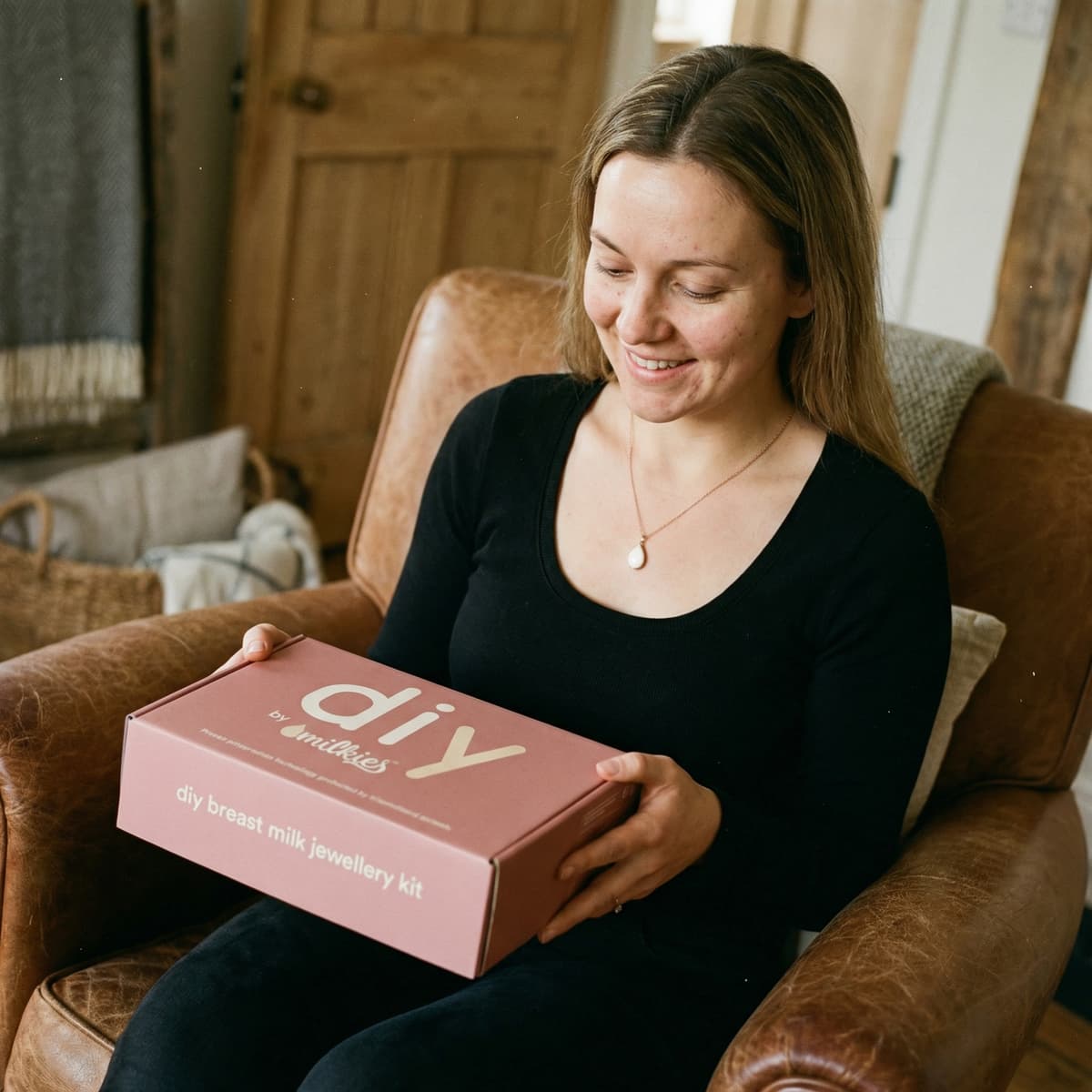 Mother unboxing the DIY by MILKIES kit at home, holding a pink “diy breast milk jewellery kit” box to create a diy breastmilk necklace keepsake with a private, hands-on process.