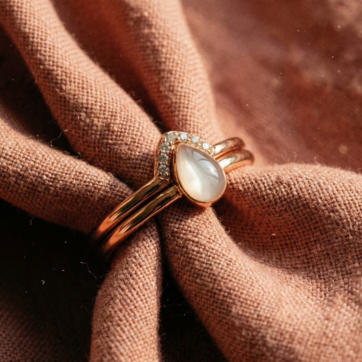 Rose gold ring made with a diy breastmilk ring kit, featuring a teardrop milky resin stone surrounded by a crystal halo on soft textured fabric