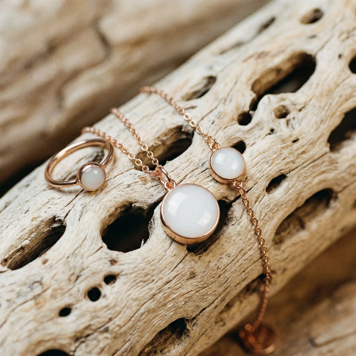 Rose gold breastmilk keepsake jewelry set with milky white resin stones—ring, necklace pendant, and bracelet—arranged on driftwood as a meaningful memento for mothers experiencing drying up milk.