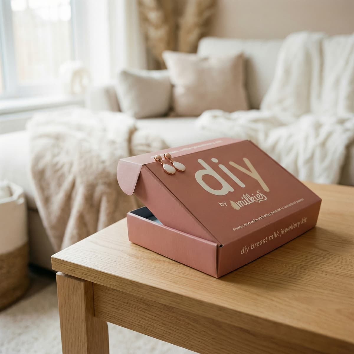 DIY by MILKIES breast milk jewellery kit box on a wooden table in a cozy living room, a thoughtful end of breastfeeding gift for making a keepsake necklace, ring or earrings at home.