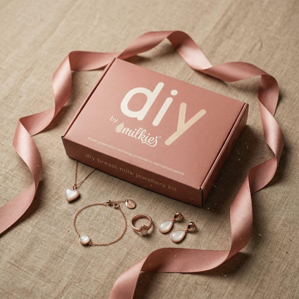 Pink DIY by MILKIES breast milk jewellery kit box tied with a satin ribbon, shown with rose-gold necklace, bracelet, ring and earrings, a meaningful gift for new mom
