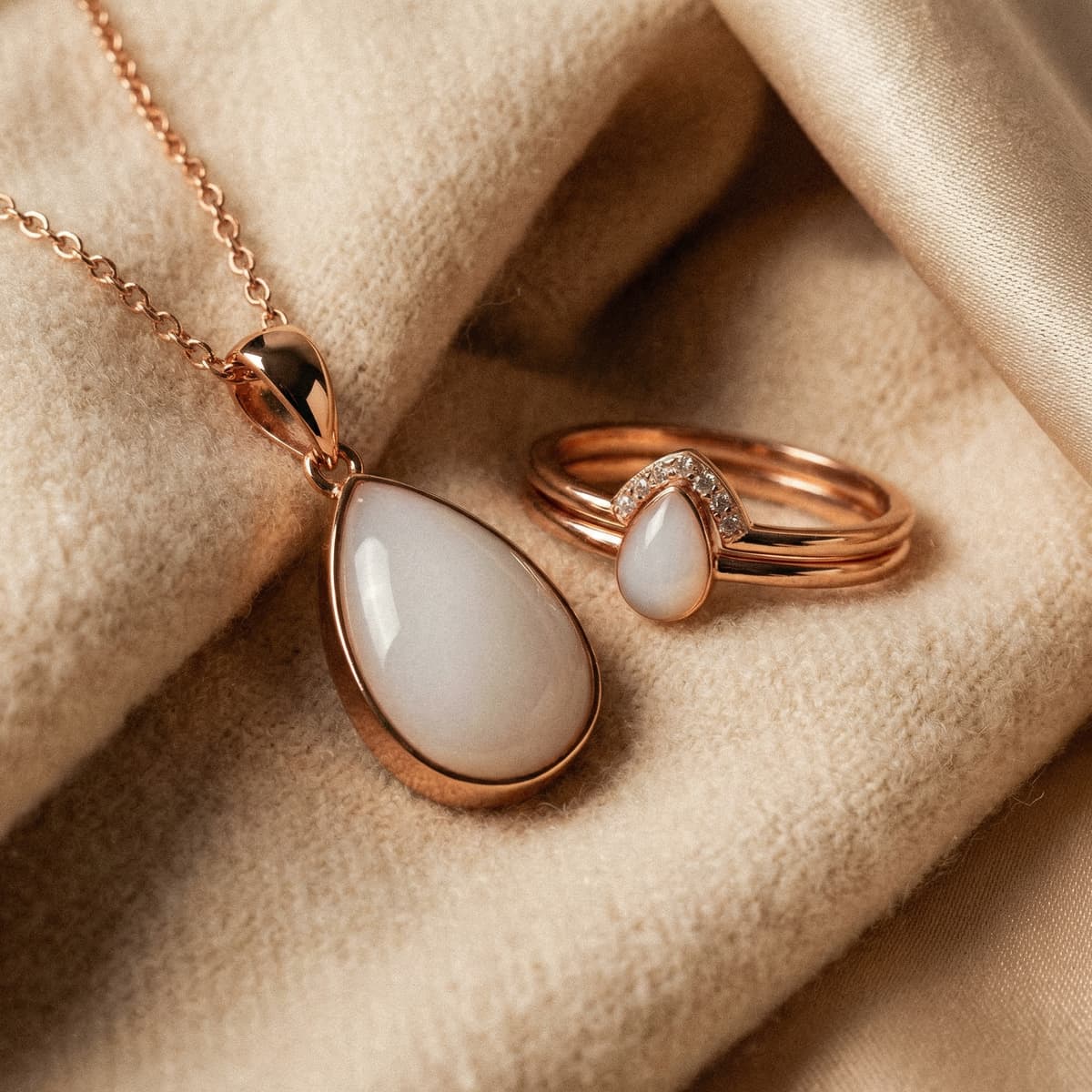Rose-gold teardrop pendant necklace and matching ring featuring milky white resin stone, an elegant last feed keepsake displayed on soft beige fabric.