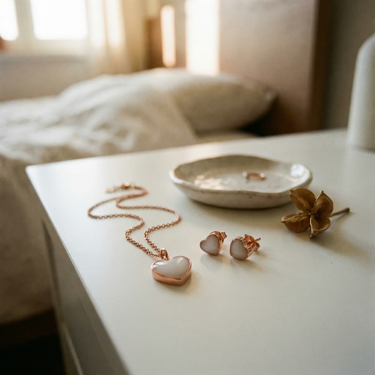 Rose-gold heart necklace with matching stud earrings on a bedside table in soft natural light, elegant milk keepsake jewelry set for preserving breastmilk memories.