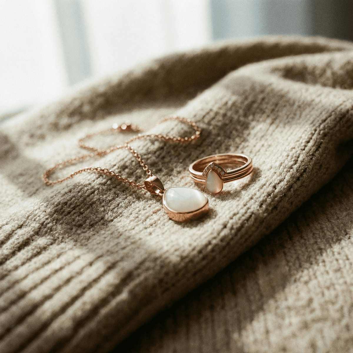 Rose gold breastmilk keepsake jewelry set for moms stopping breastfeeding, featuring a teardrop pendant necklace and matching ring with milky white stone on a beige knit sweater.