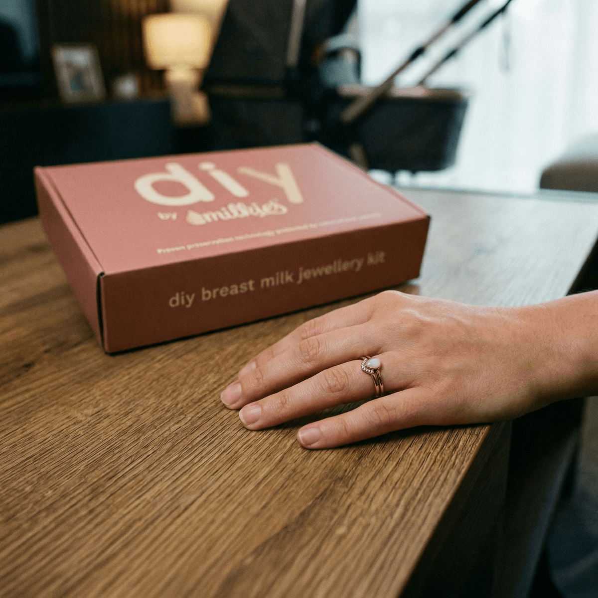 DIY by MILKIES breast milk jewellery kit box on a wooden table next to a mother’s hand wearing a keepsake ring, highlighting unique push presents for new moms