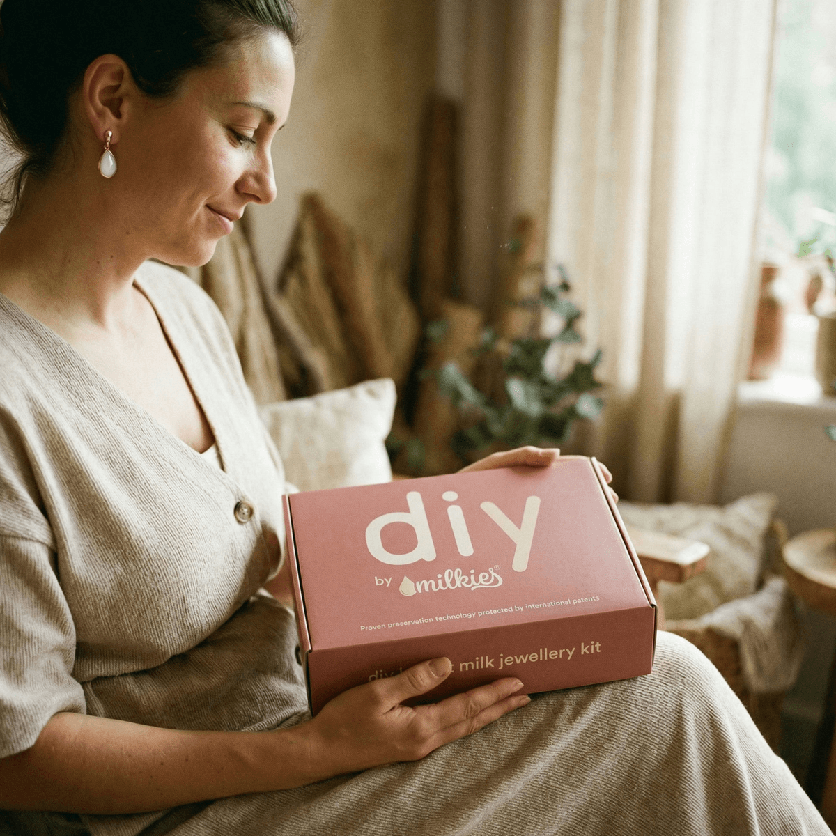 Mother holding DIY by MILKIES breastmilk jewellery kit box at home, presenting it as a thoughtful weaning gift and explaining why the patented preservation technology makes an at-home keepsake a smart choice.