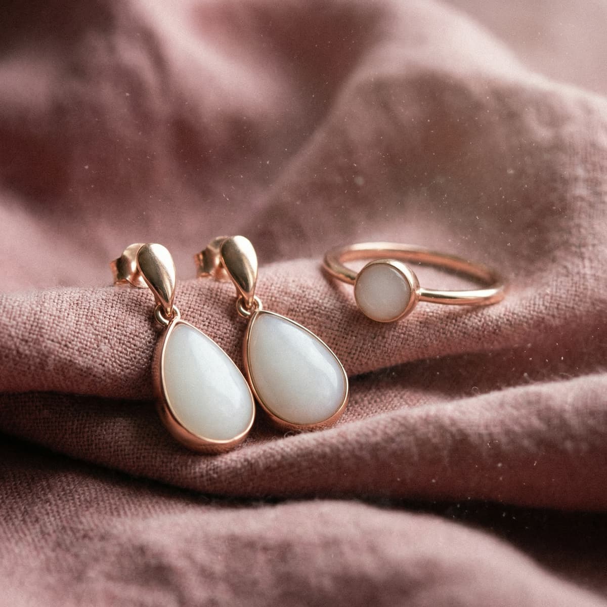 Rose-gold ring and teardrop earrings with milky white resin stones on soft fabric, showcasing keepsakes made with a breast milk jewellery making kit.