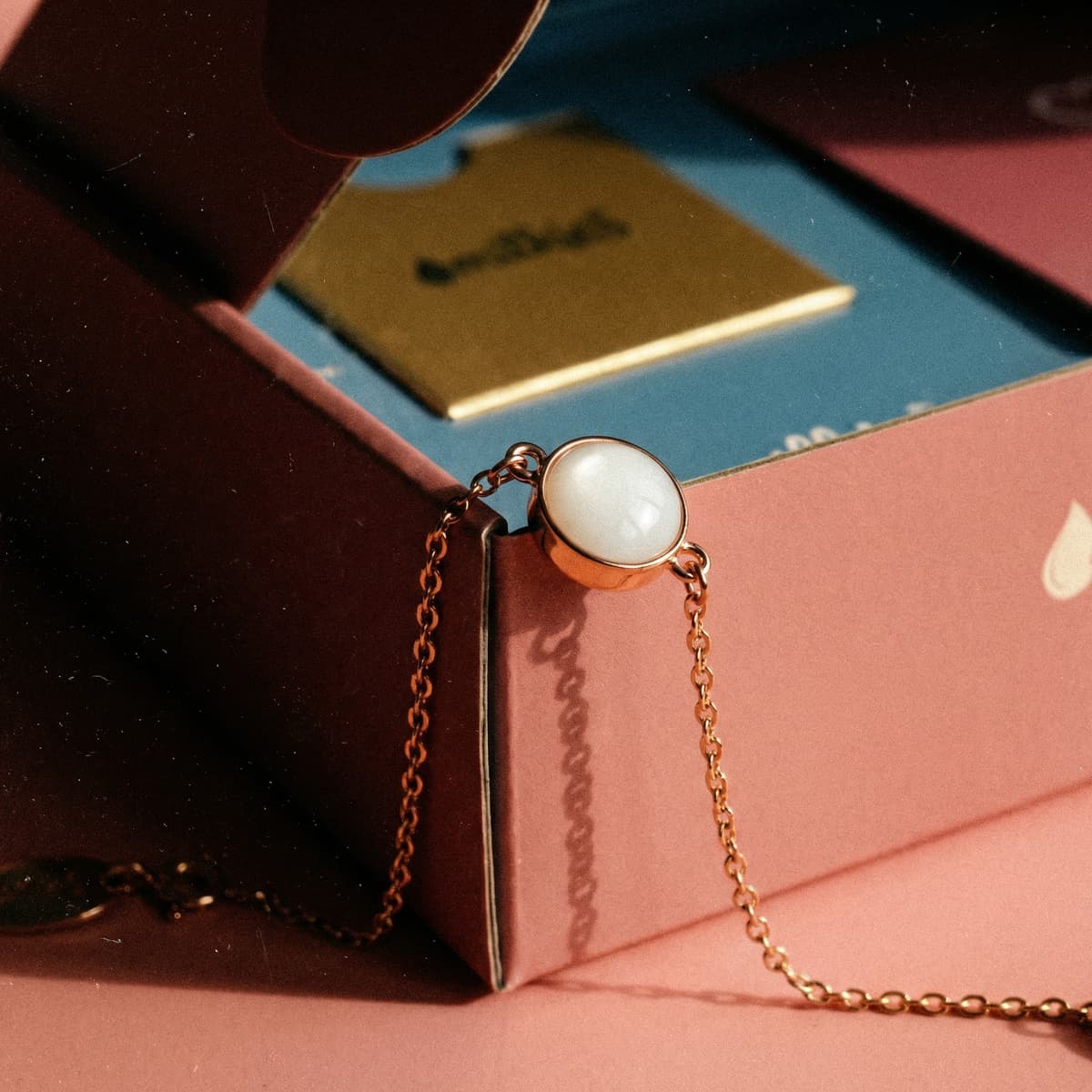 Rose-gold chain bracelet with milky white resin charm displayed on a pink DIY by MILKIES box, highlighting a breastmilk bracelets diy making kit for keepsake jewelry crafting.
