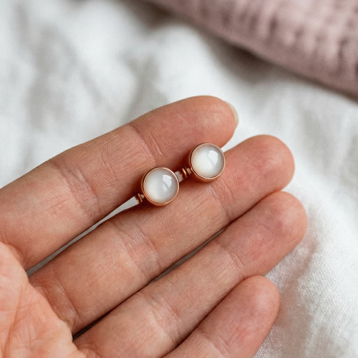 Rose gold stud earrings with milky white resin stones held in a hand, created using a breastmilk earring diy making kit for a DIY keepsake jewelry project.
