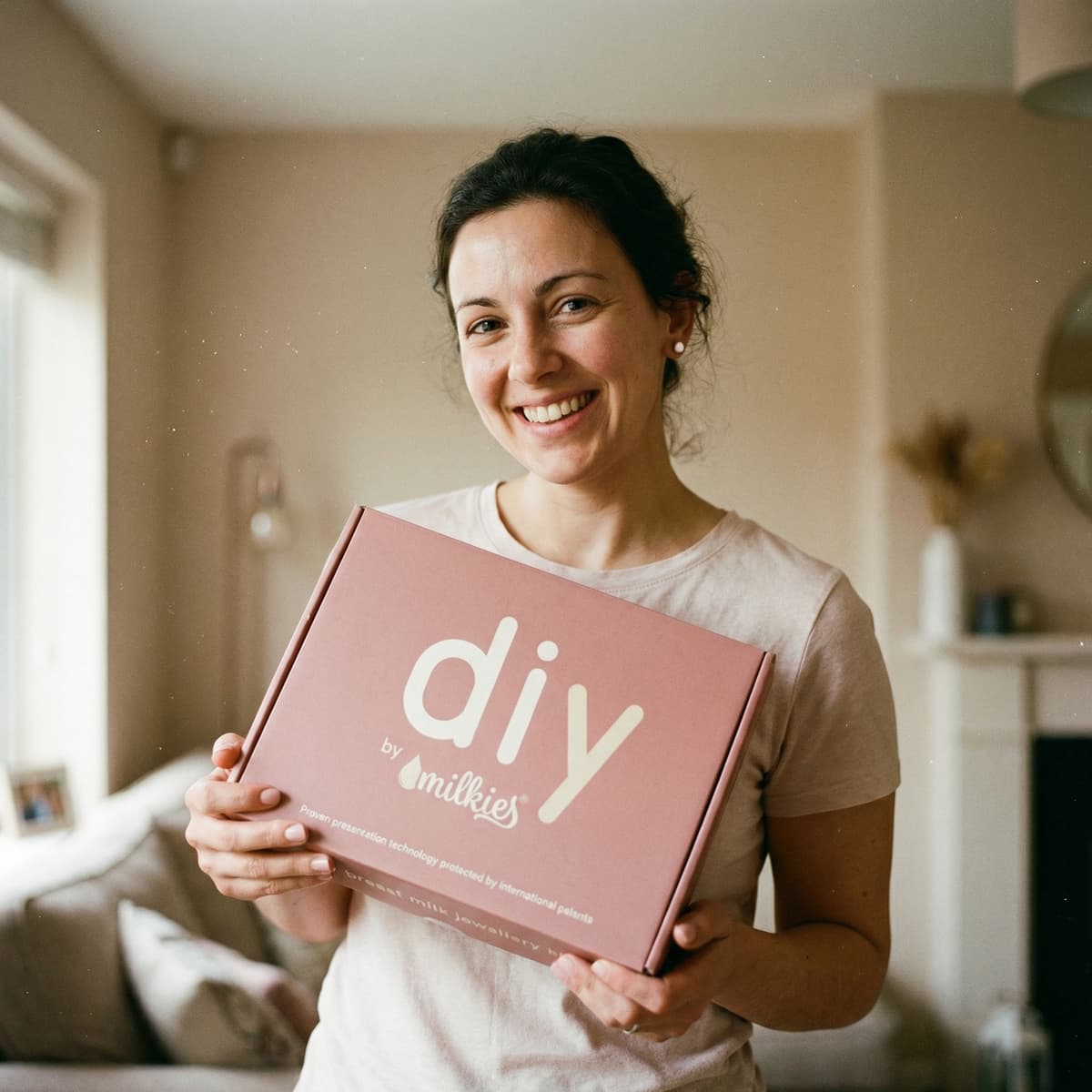 Smiling mom at home holding a DIY by MILKIES box, showing why choosing a breastmilk earring diy making kit is a convenient, trusted way to create a personal keepsake in private.