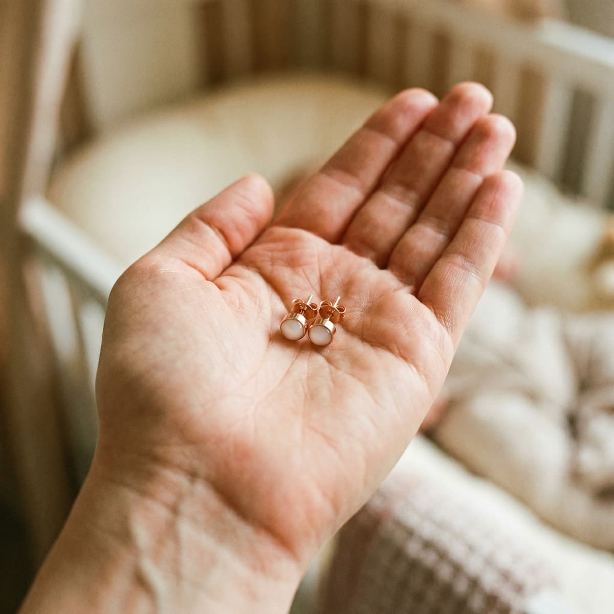 Rose-gold stud earrings with milky white resin stones displayed in an open palm, showing finished keepsakes made from a breastmilk earrings diy making kit in a cozy home setting.