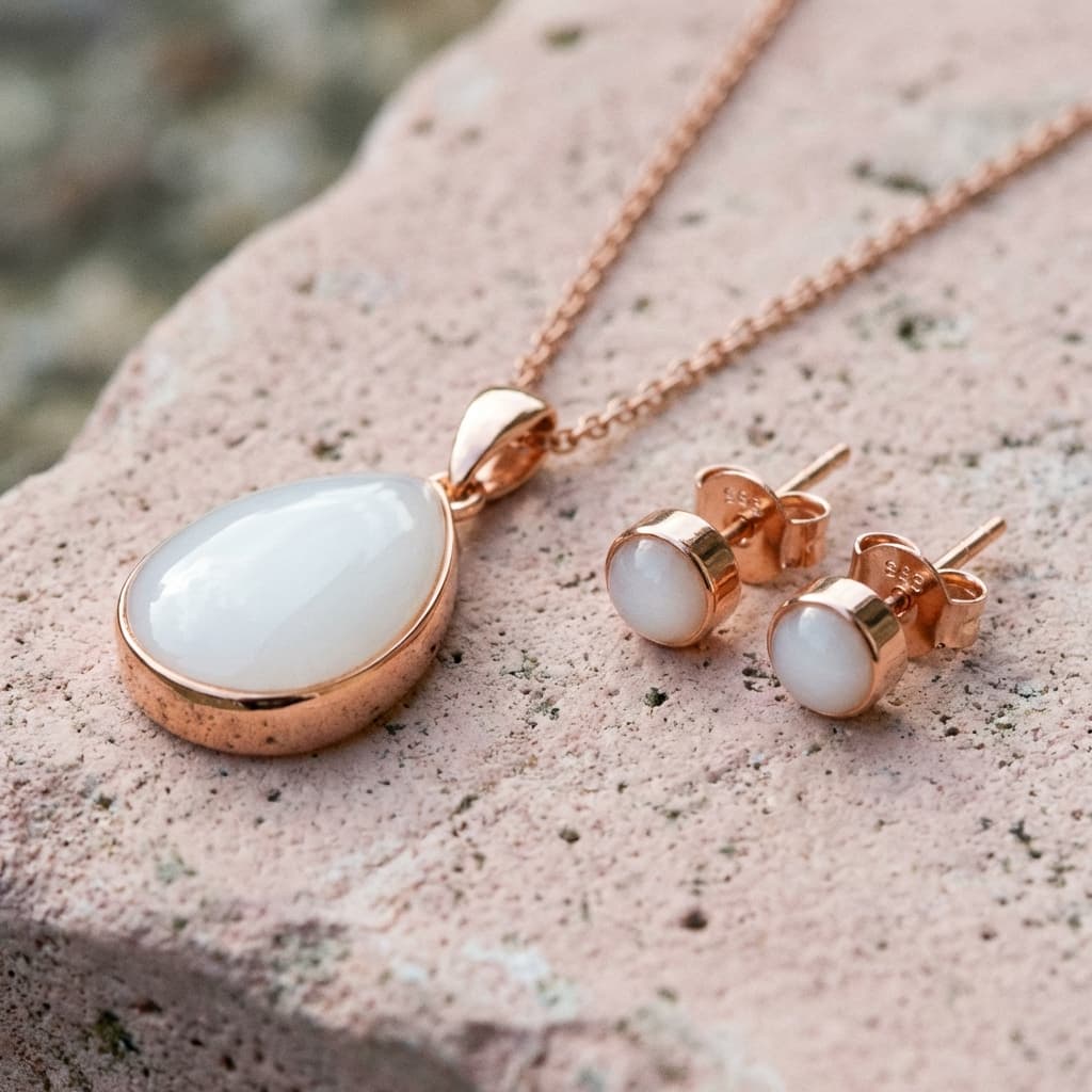 Rose gold necklace pendant and matching stud earrings with milky white resin stones, an elegant keepsake made using a breastmilk jewelry diy kit, displayed on a textured stone surface.