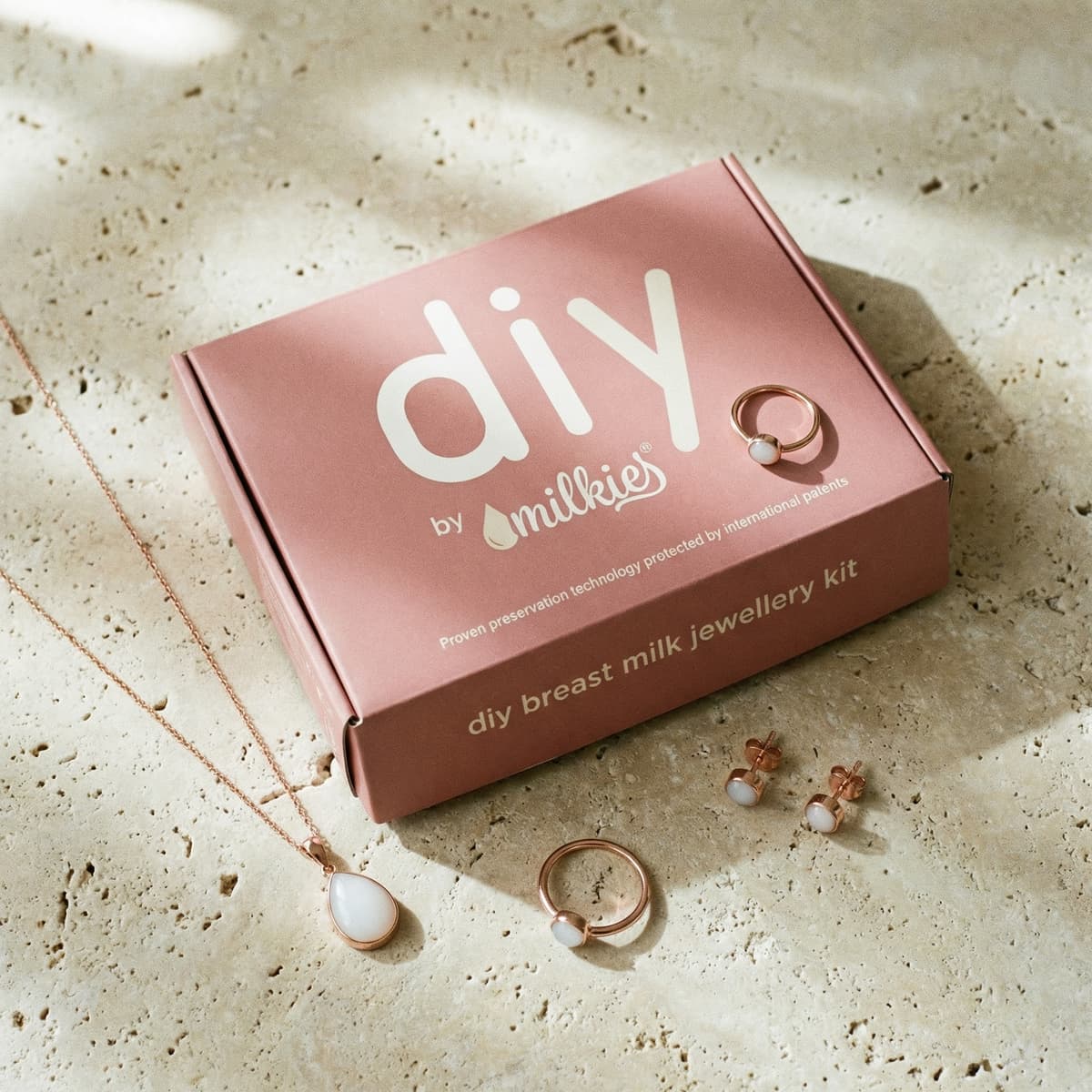 Flat lay of a DIY by MILKIES box with necklace, ring, and stud earrings, showcasing a breastmilk jewelry diy resin kit for creating breast milk keepsake jewelry at home.