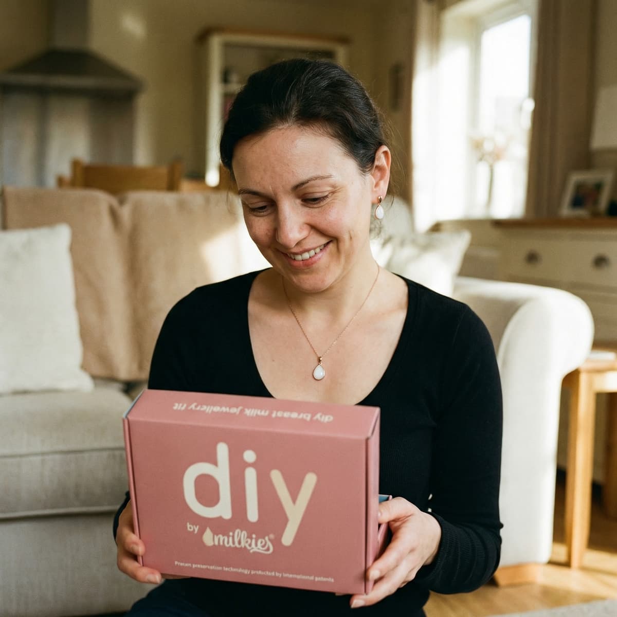 Smiling mom at home holding a DIY by MILKIES box, showing why a breastmilk necklaces diy making kit is a convenient, private way to create a lasting breastmilk keepsake.