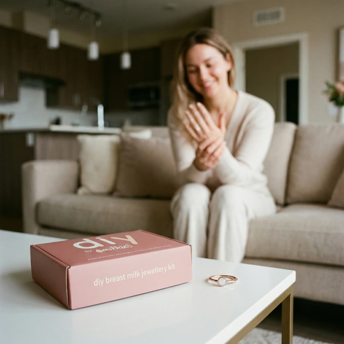 Milkies DIY box on a coffee table with a ring, showcasing a diy breast milk jewellery kit as a woman admires her keepsake in a cozy home setting.