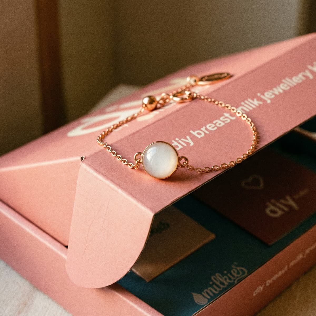 Rose-gold bracelet with a milky white resin charm displayed on a pink DIY by MILKIES box, showcasing a diy breastmilk bracelet making kit for creating keepsake jewelry at home.