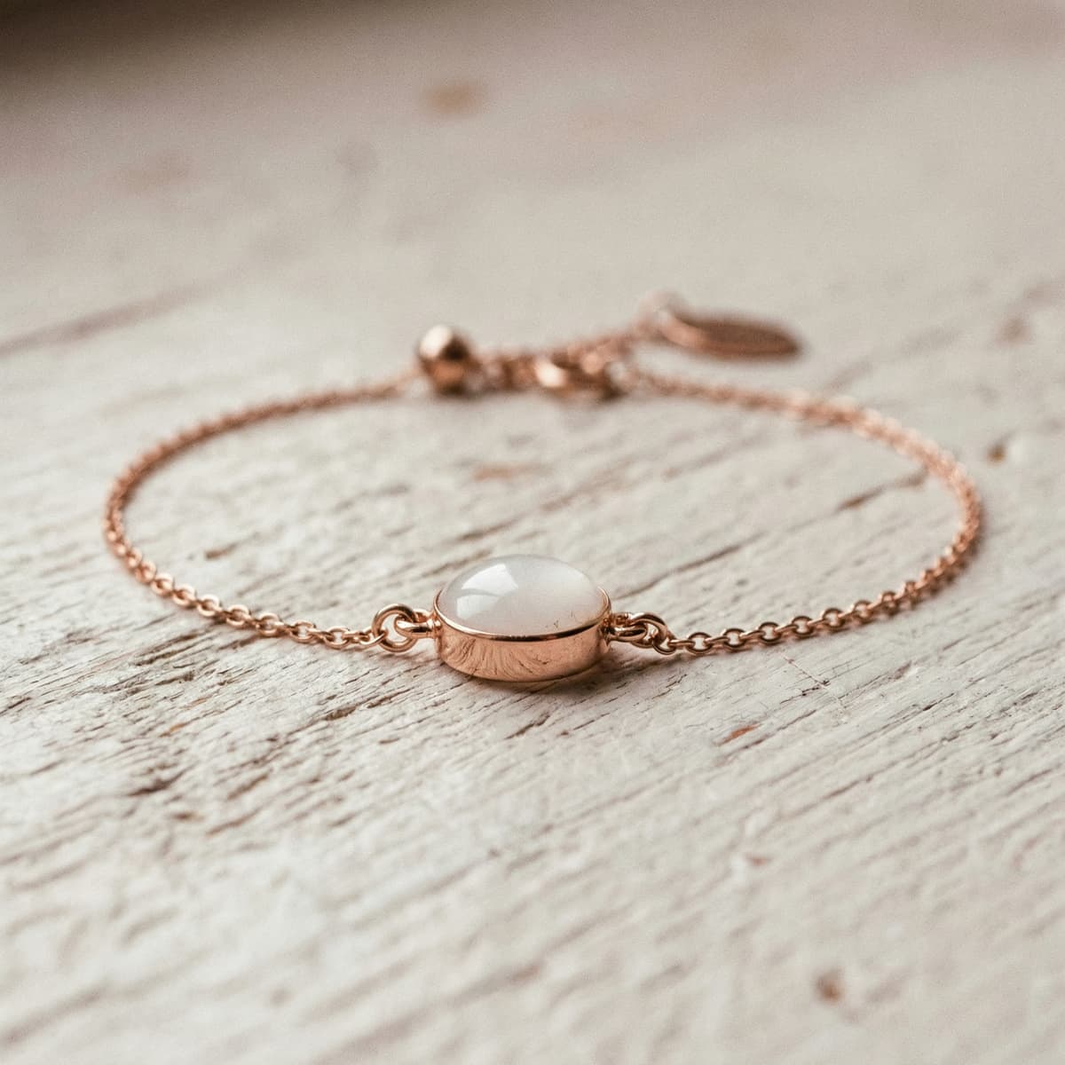 Rose gold chain bracelet with an oval white resin stone centerpiece, finished keepsake made using a diy breastmilk bracelet making kit, photographed on a rustic wood surface.