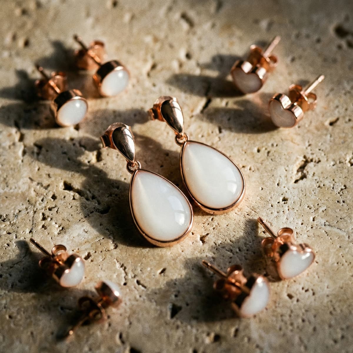 Rose gold teardrop and heart stud earrings with milky white resin stones, finished keepsakes made using a diy breastmilk earring making kit on a textured stone surface.