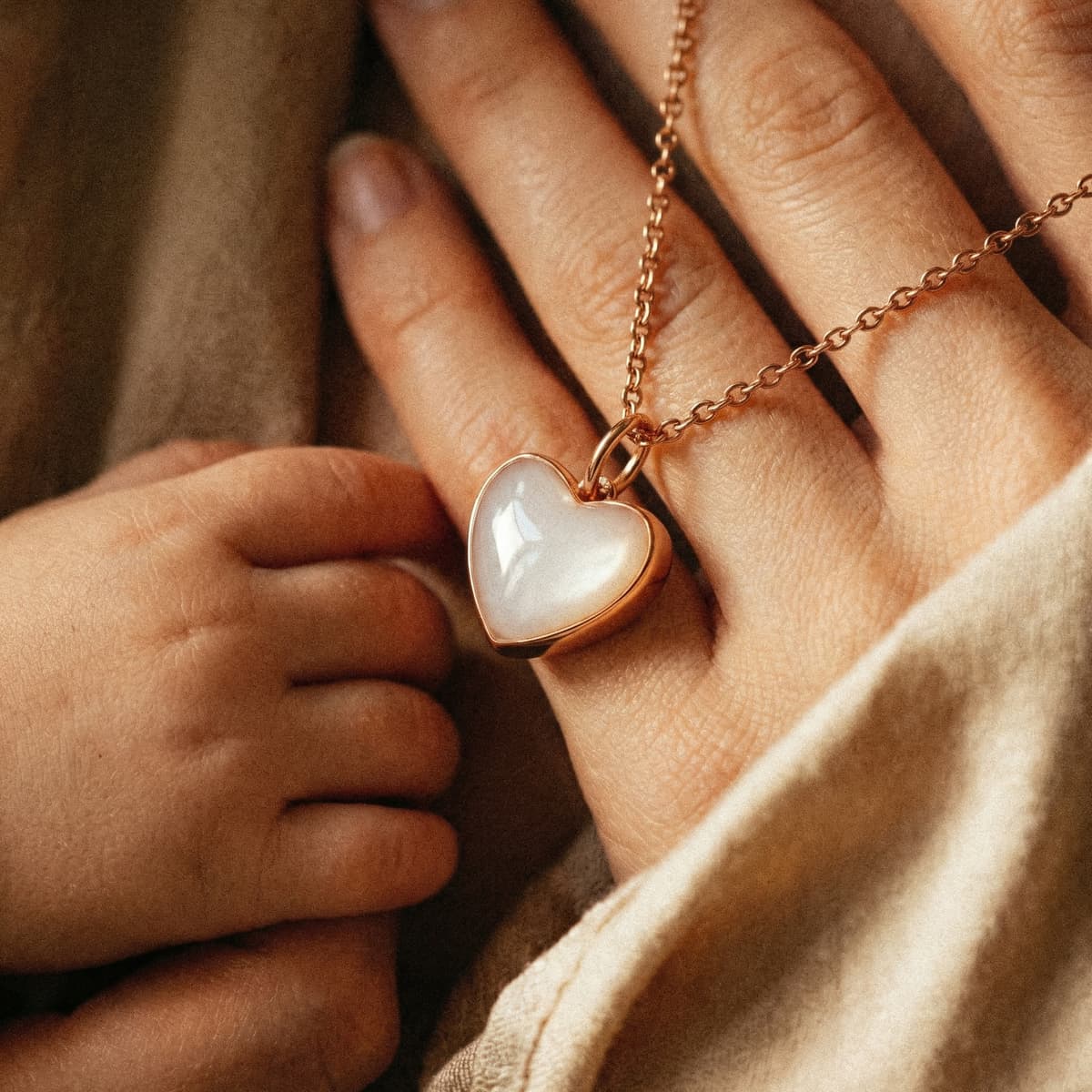 Mother and baby hands holding a rose-gold heart pendant keepsake made with a diy breastmilk necklace kit in a warm, cozy close-up setting.