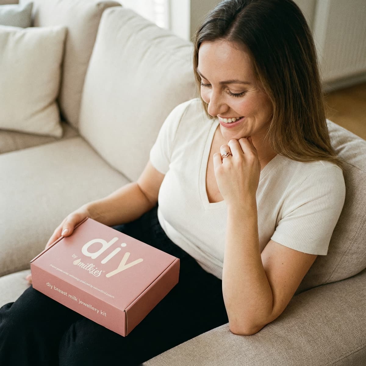Smiling mom at home holding a pink DIY by MILKIES box, highlighting why an at-home diy breastmilk ring making kit is an easy, private way to create a meaningful keepsake jewelry piece.